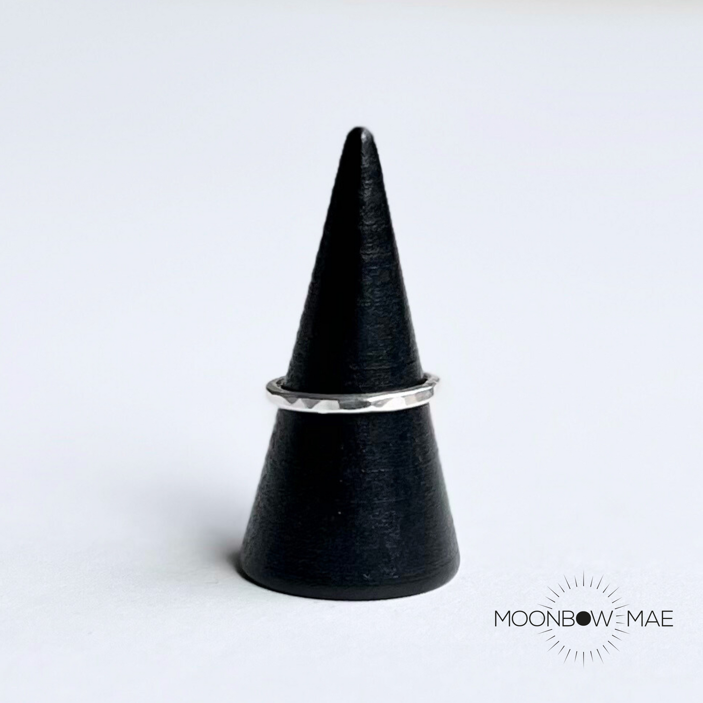 Moonbow Mae handmade hammered silver stacking ring resting on black cone